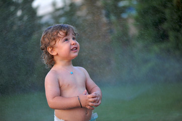 Baby getting wet on a garden in summer