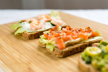 Open sandviches with guacamole, fish and prawn on wood texture  background