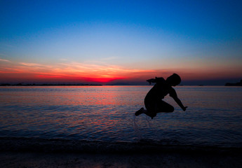 Boy jumping in holiday with sunset on the beach background