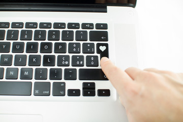 Technology also applies to emotional relationships: a woman's hand is about to press a key on a laptop keyboard with a stamped heart