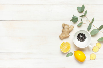 Fresh ginger root, cup tea with brewing inside, lemon, eucalyptus leaves on white wooden...