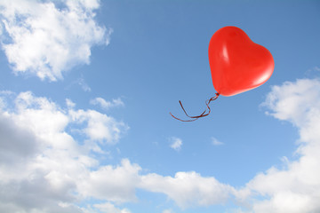 red heart shaped balloon flies into the blue sky with clouds, love concept, copy space