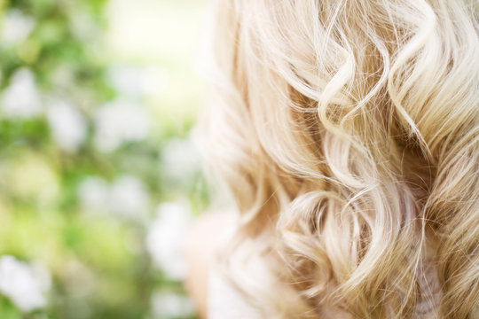 Fashion photo of beautiful young woman  posing in garden with blossom trees. Blonde in flowering gardens. Beautiful streaming blonde curls.  View from a back. Close up picture