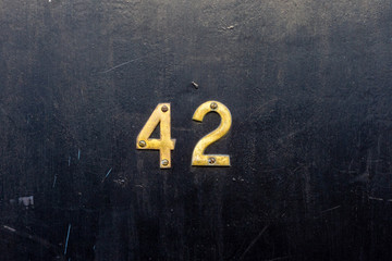House number 42 with the forty two in bronze lettering on a black wooden door - obrazy, fototapety, plakaty
