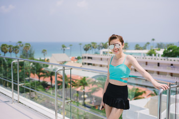 Outdoor summer portrait of young stylish fashion glamorous asian woman posed in sunny day swimsuit and sunglasses standing near swimming pool.