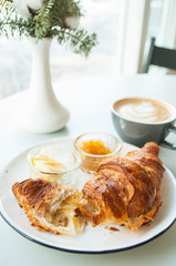 Fresh croissant with jam and butter and cappuccino with beautiful latte art in a cafe. Fresh breakfast.