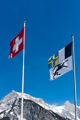flags of Switzerland and the Grisons canton blowing in the wind in a blue sky in the mountains