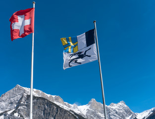 flags of Switzerland and the Grisons canton blowing in the wind in a blue sky in the mountains