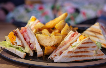 Club sandwich, take away food. Toasted bread slices, cheese, ham, egg, lettuce, french fries, closeup