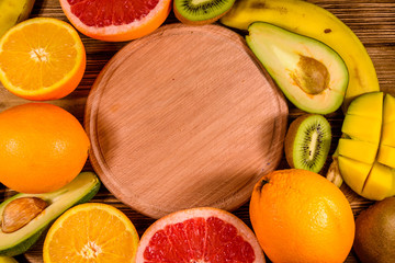 Still life with exotic fruits and cutting board. Bananas, mango, oranges, avocado, grapefruit and kiwi fruits on wooden table. Top view