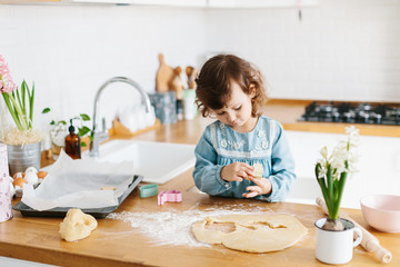 Little girl preparing easter cookies at the kitchen.