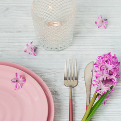 Pink rustic table setting with purple hyacinth flower, candles and linen napkin on white wooden table