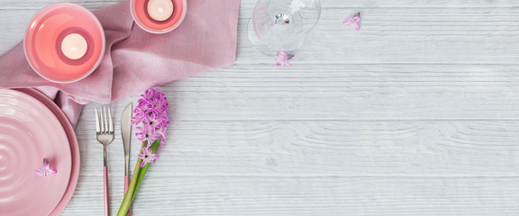 Pink rustic table setting with purple hyacinth flower, candles and linen napkin on white wooden table