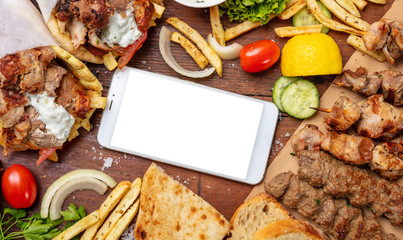Gyro pita, shawarma, online order. Two wraps with meat, and blank screen mobile phone on wooden table