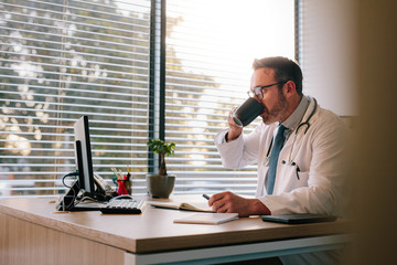 Doctor working at his office desk and drinking coffee