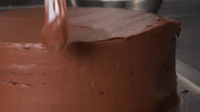 Chocolate frosting is smoothed out on the side of a cake base with a knife - closeup