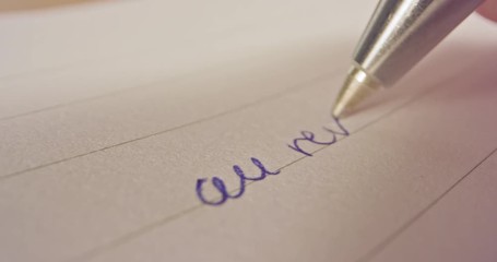 Sliding macro shot of a pen tip writing French words on paper