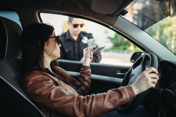 Male cop in uniform writes a fine to female driver - obrazy, fototapety, plakaty