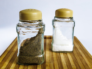 Salt and pepper in a glass shaker and pepper shaker stand on a cutting board