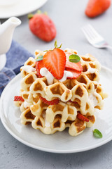 Belgium waffles topped with cream and fresh strawberries.