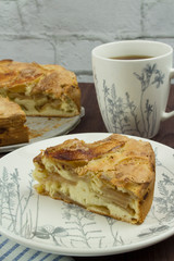 A piece of American apple pie on a white plate with a large white cup of tea