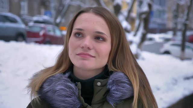 Closeup portrait of young attractive brunette caucasain female smiling and looking at camera in contemplation in a showy winter day