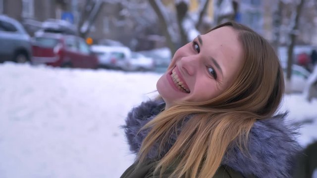 Closeup shoot of young beautiful caucasian brunette female being happy and jumping from joy laughing and turning around looking at camera in a snowy day