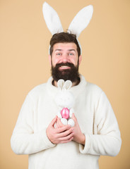 The arrival of spring. Bearded man with bunny toy and Easter egg. Celebration of spring time holiday. Easter bunny delivering colored eggs. Hipster with long rabbit ears holding egg laying hare