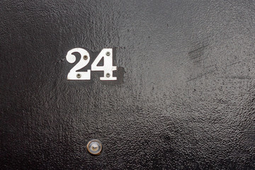 House number 24 with the twenty four in silver on a black door with peephole