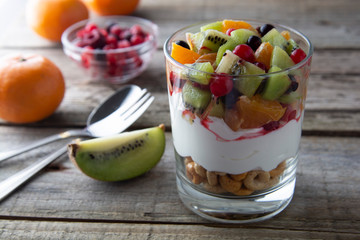 Fresh fruit salad with yogurt and walnuts in glass bowl on stone background. Healthy Eating. Selective focus.