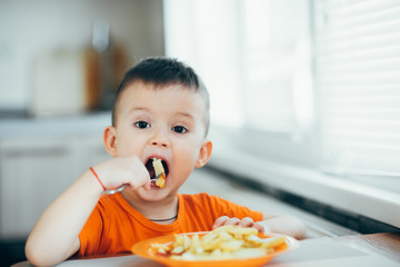 beautiful baby in orange t-shirt with orange plate eating fried French fries