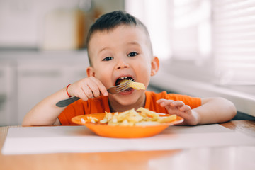 beautiful baby in orange t-shirt with orange plate eating fried French fries