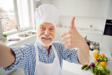 Close up photo cheer grey haired he his him grandpa telephone make take selfies thumb up great quality advising followers wear baker chefs costume casual checkered plaid shirt outfit house kitchen