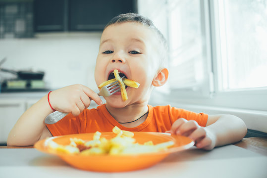 Beautiful Baby In Orange T-shirt With Orange Plate Eating Fried French Fries