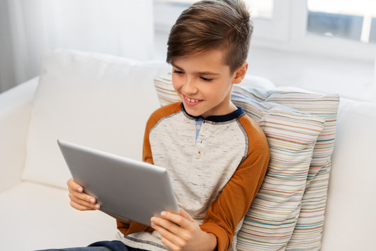 childhood, technology and people concept - smiling boy with tablet pc computer sitting on sofa at home