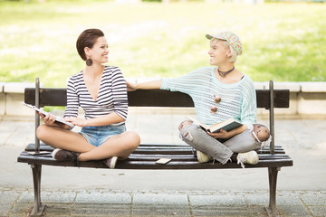 Young beautiful students(one with flower tights) sitting on a bench in campus and laughing