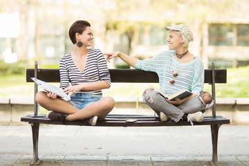Young female students sitting(one with flower tights) on a bench in campus and laughing