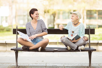 Young beautiful students(one with flower tights) sitting on a bench in campus and laughing