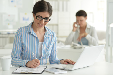Fototapeta premium Portrait of young attractive woman working with laptop in office