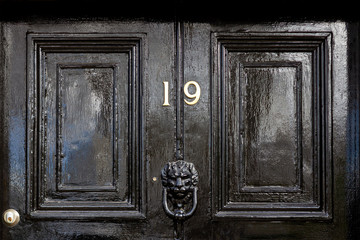 House number 19 in bronze on a black wooden entrance door with the nineteen in bronze numerals and...