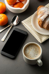 Fototapeta na wymiar Delicious breakfast coffee with croissant and citrus fruits. Heart shaped box. Work table with smart phone. French pastry and cup of coffee. Template for social media. Copy space.