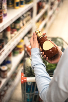 Woman choosing bottle of sauce at supermarket.