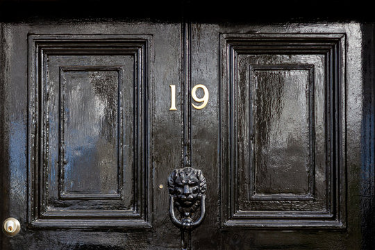 House number 19 in bronze on a black wooden entrance door with the nineteen in bronze numerals and a black lions head door knocker
