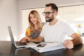 Amazing happy young loving couple sitting at the kitchen using laptop computer.