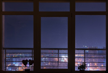 Beautiful night city view from cosy panoramic window with rain drops on it. Kyiv, Ukraine.