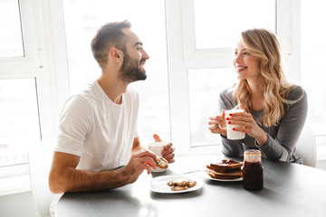 Young loving couple sitting at the kitchen have a breakfast talking with each other.