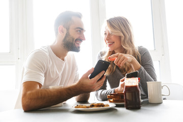 Loving couple sitting at the kitchen have a breakfast using mobile phones.