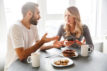 Loving couple sitting at the kitchen have a breakfast using mobile phone.