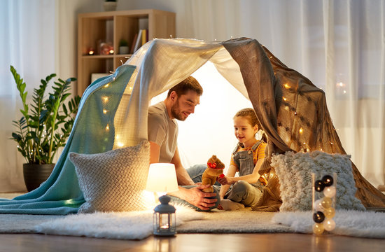 Family, Hygge And People Concept - Happy Father With Teddy Bear Toy And Little Daughter Playing In Kids Tent At Night At Home