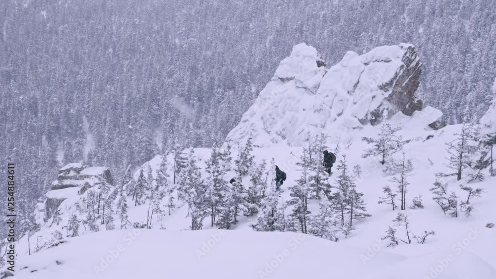 Wall mural A group of tourists with backpacks on their shoulders descends from the top of a snow-covered mountain. Slow motion.